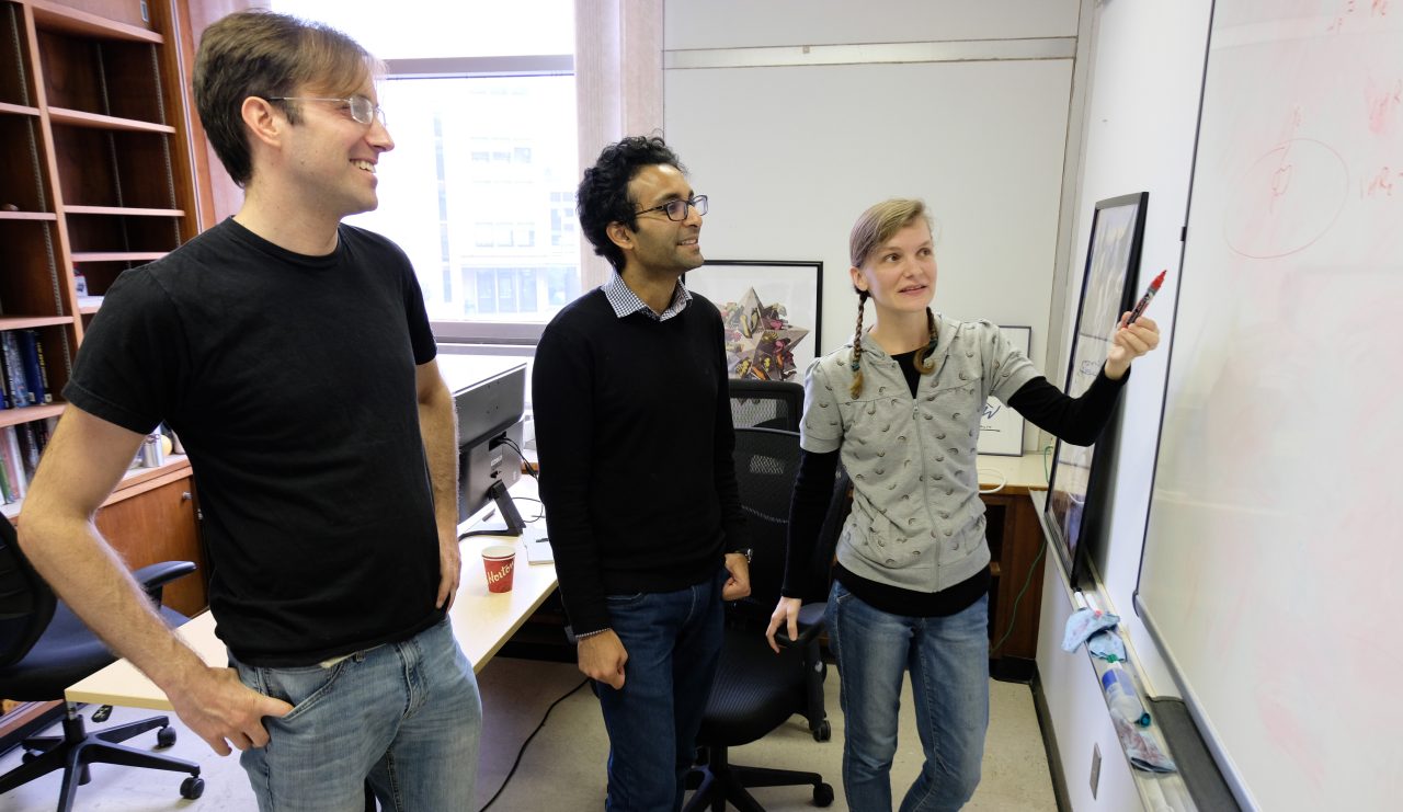 three people standing at a whitboard pointing at something