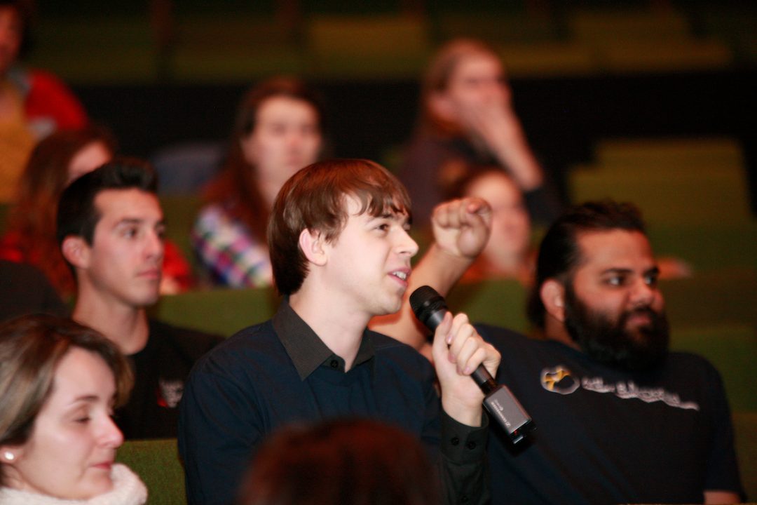 An audience member speaks into a microphone while other audience members look towards the stage.