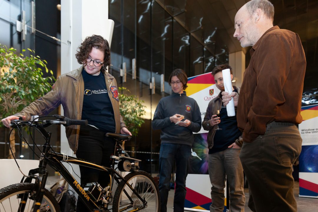 Laura gestures to a bike while three people watch.