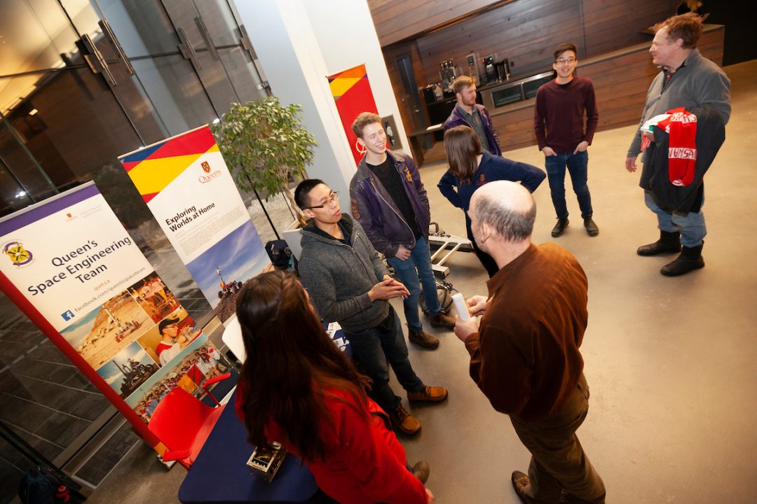 Students representing the Queen's Space Engineering Team speak to people while standing in front of signs with information about the club.