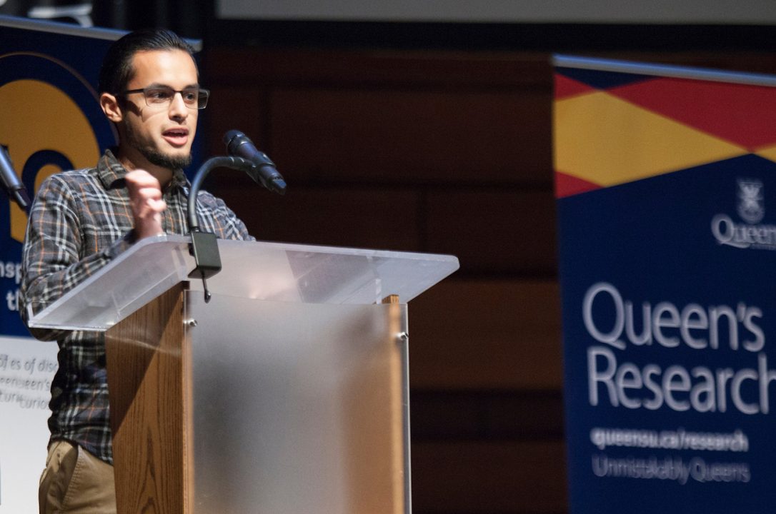 Hector speaks into a microphone while standing at a podium. A sign that reads 