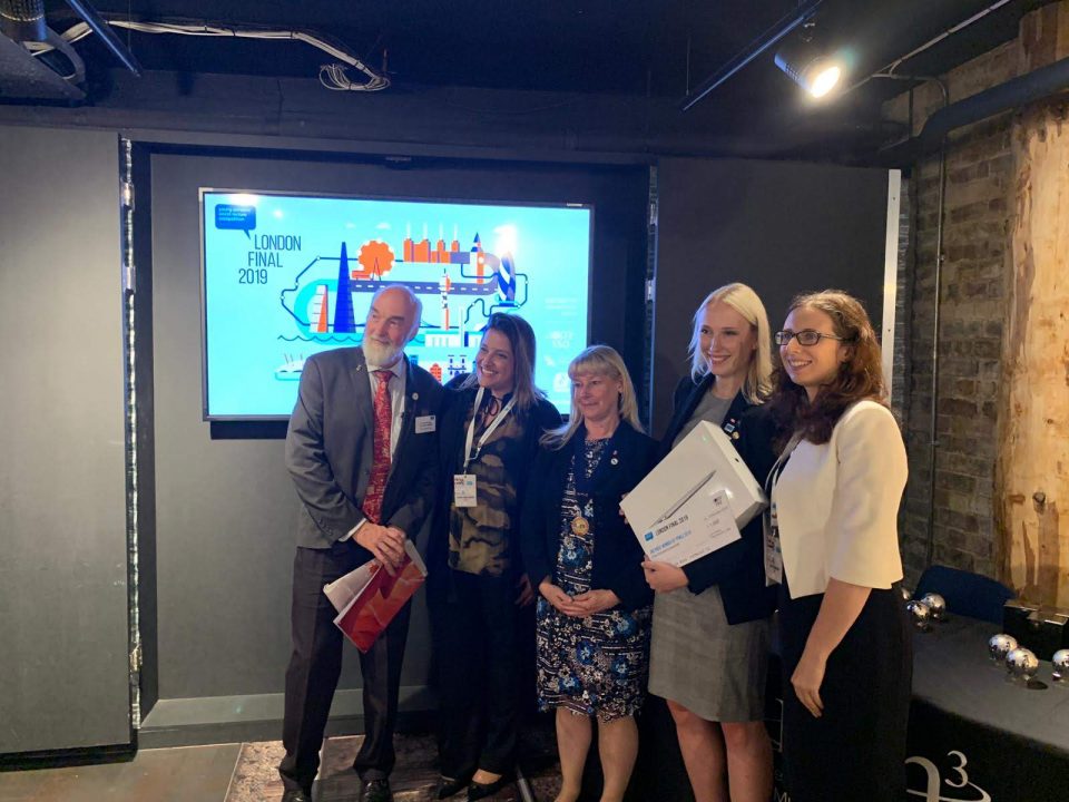 Morgan Lehtinen holds up a box and a cheque while posing with four other people below a screen reading 