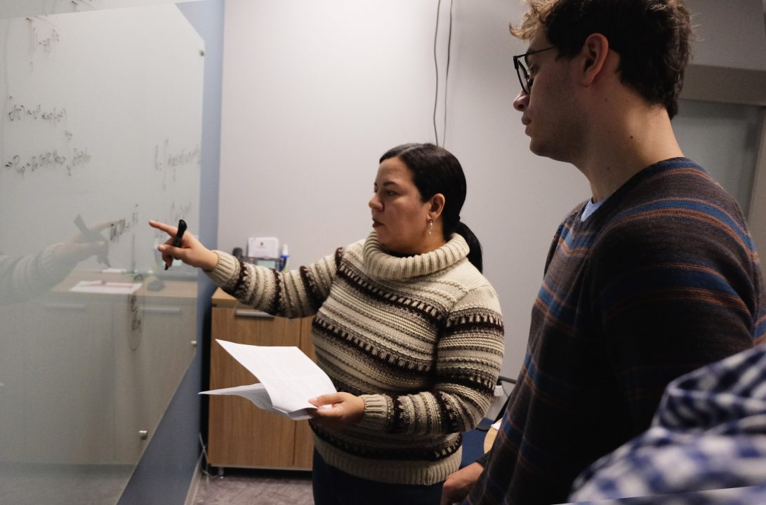 Elaine Fortes points at writing on a whiteboard while Alan Goodman watches