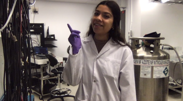 Melissa Medina-Peregrina is shown wearing a lab coat and goggles inside a research facility, next to a gas cylinder and many wires