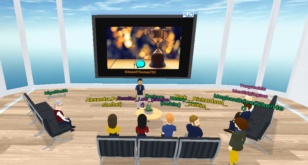 A digital meeting room includes benches and a presentation screen. Several digital characters sit on the benches watching the presentation, while one character presents