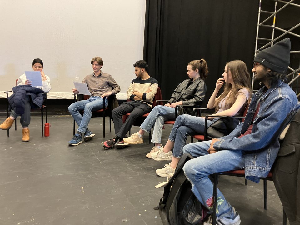 a photo of a group of students sitting around a circle reading scripts
