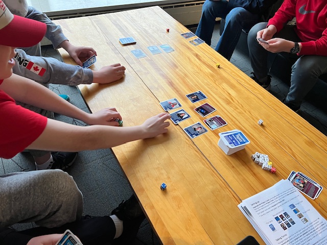 Kids sitting at a table playing a card game.