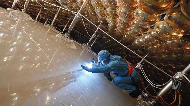 A scientist wearing a blue clean-suit shines a light on the outside of the JUNO detector